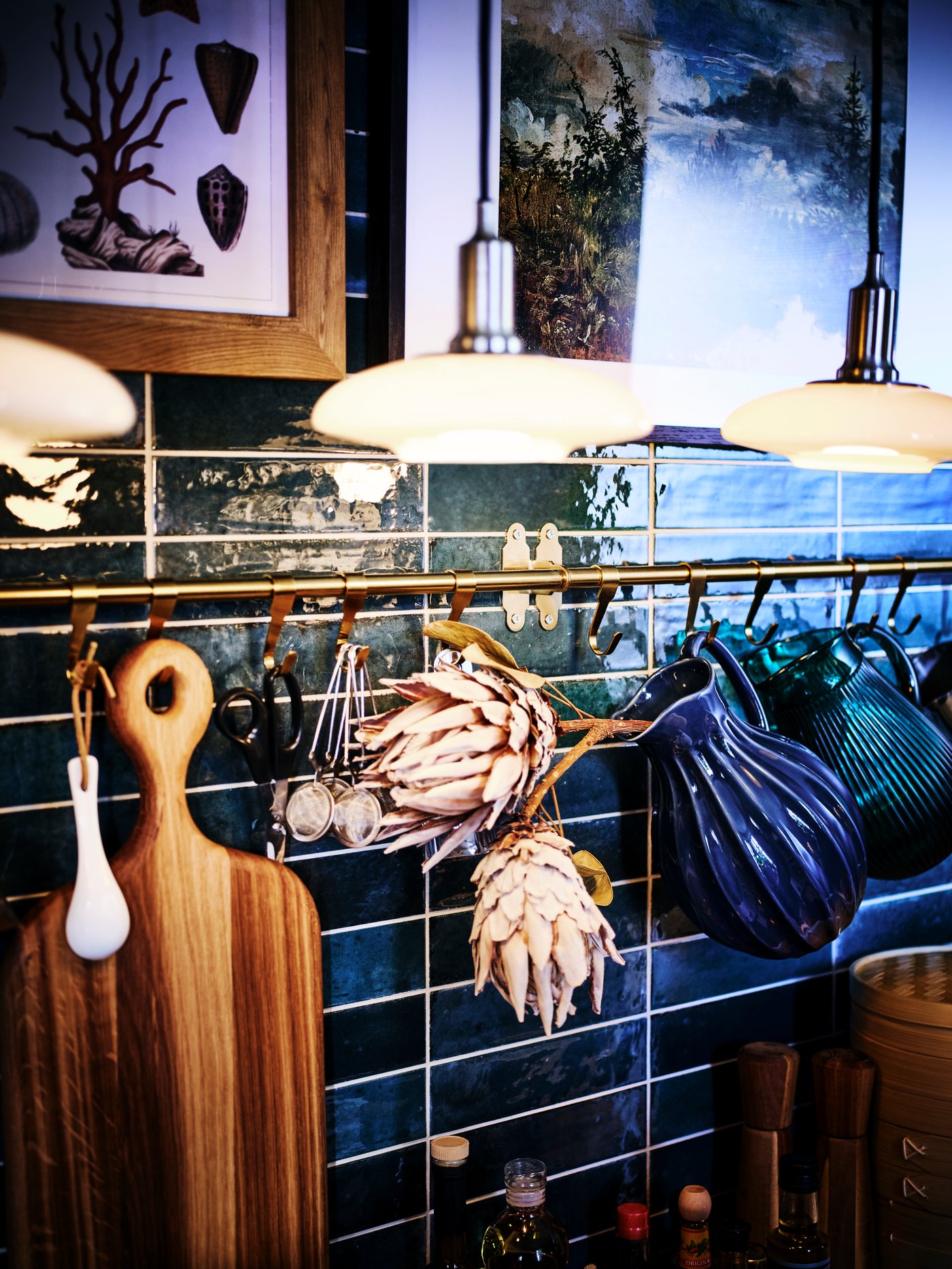 A blue tiled kitchen wall with HULTARP rails and brass hooks carrying jugs, a chopping board and scissors.
