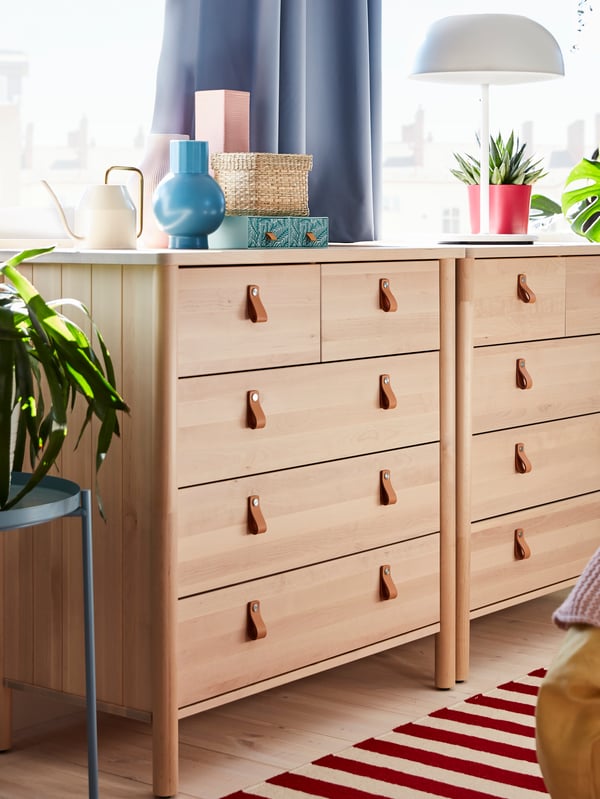 Two BJÖRKSNÄS chests of drawers side-by-side in front of a window, with small baskets, plants and a white lamp on top.