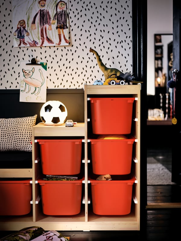 A toy-filled TROFAST unit with orange storage boxes in a kids’ room set in an otherwise black-and-white colour scheme.