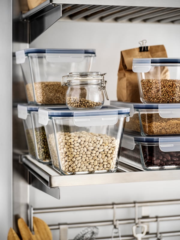 Verschiedene Trockenvorräte – Bohnen, Linsen, Getreide – in IKEA 365+ Glasbehältern auf einem Metallregal in einer Küche.