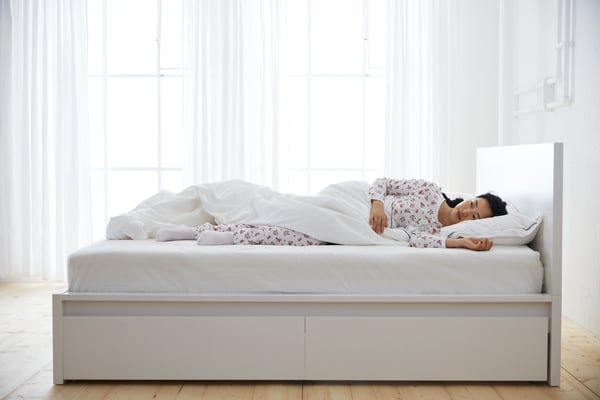 Una donna che riposa su un letto bianco con un materasso e e cuscino bianchi.