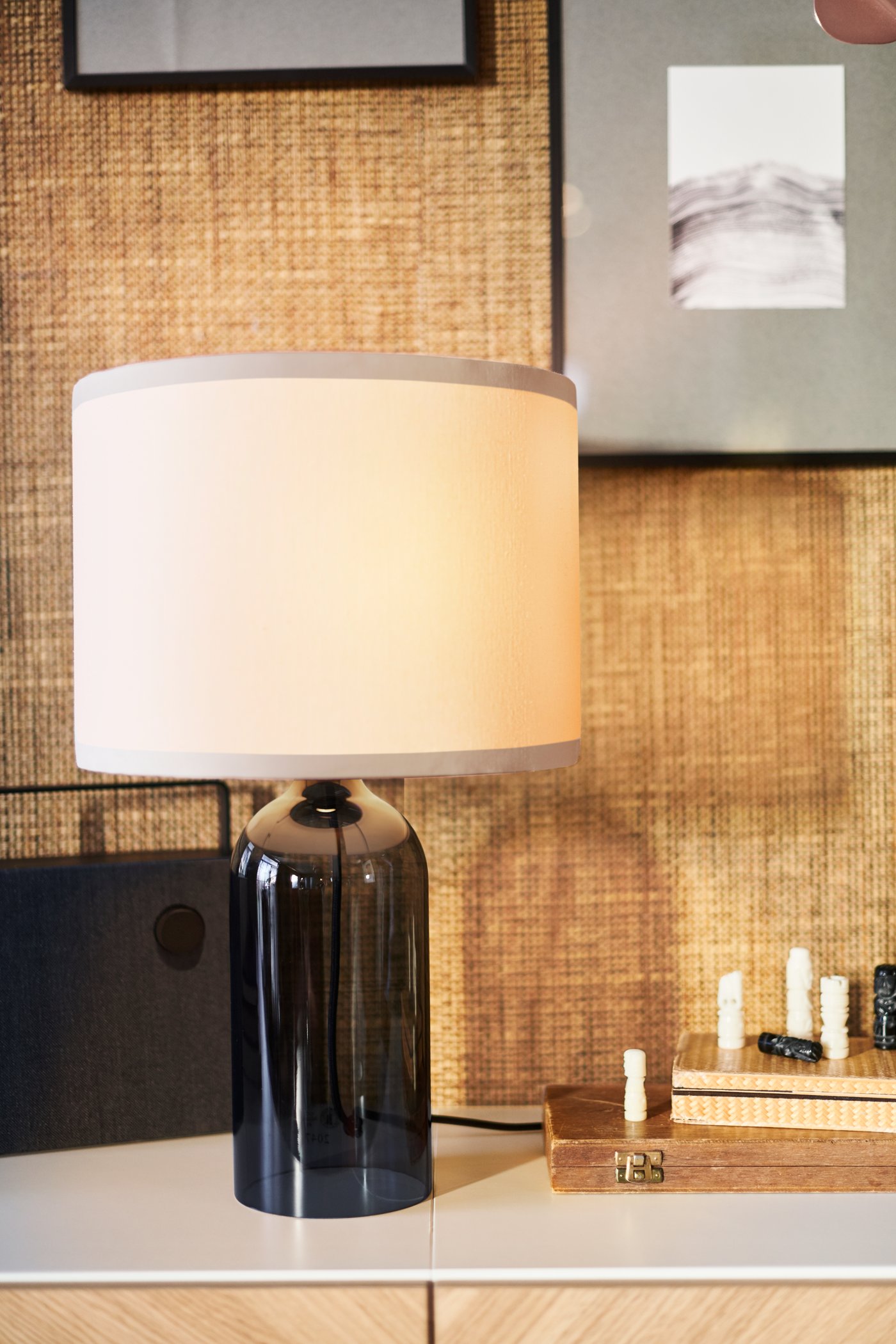 En TONVIS bordslampa med svart glasfot ochen ljusbeige tygskärm.
