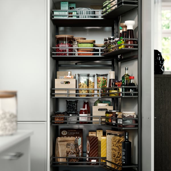 A pantry with UTRUSTA pull-out larder, neatly stacked with jars, bottles, pasta, sauces, and wooden boxes on the shelves.