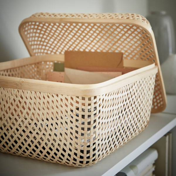 Woven bamboo box with open lid and small objects inside.