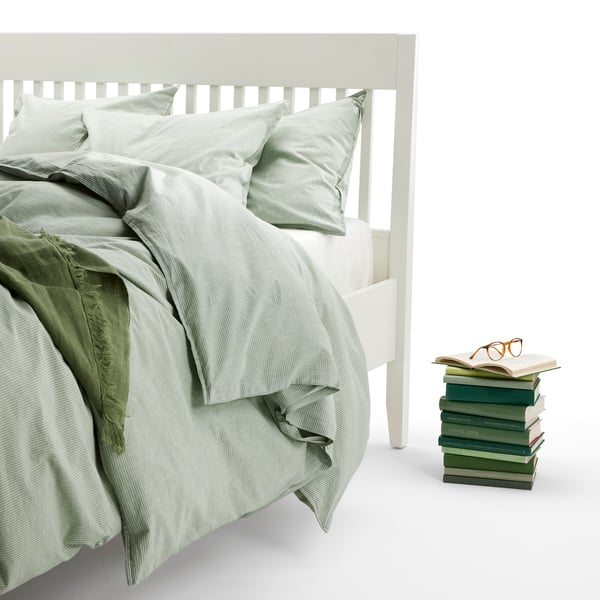 Ein IDANÄS Bett ist in einem hellen Studio zu sehen, darauf liegt eine grüne BERGPALM Bettwäsche.