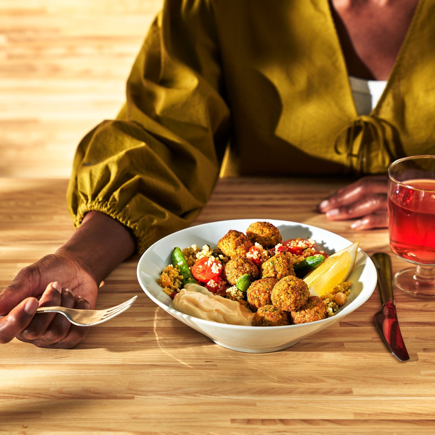 A lady sitting at a table, enjoying a delicious meatballs meal and a fruity soft drink.
