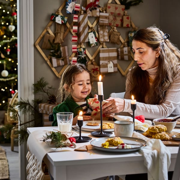 Mesa de comedor HAUGA blanca con decoración navideña y una mujer con su hija decorando.