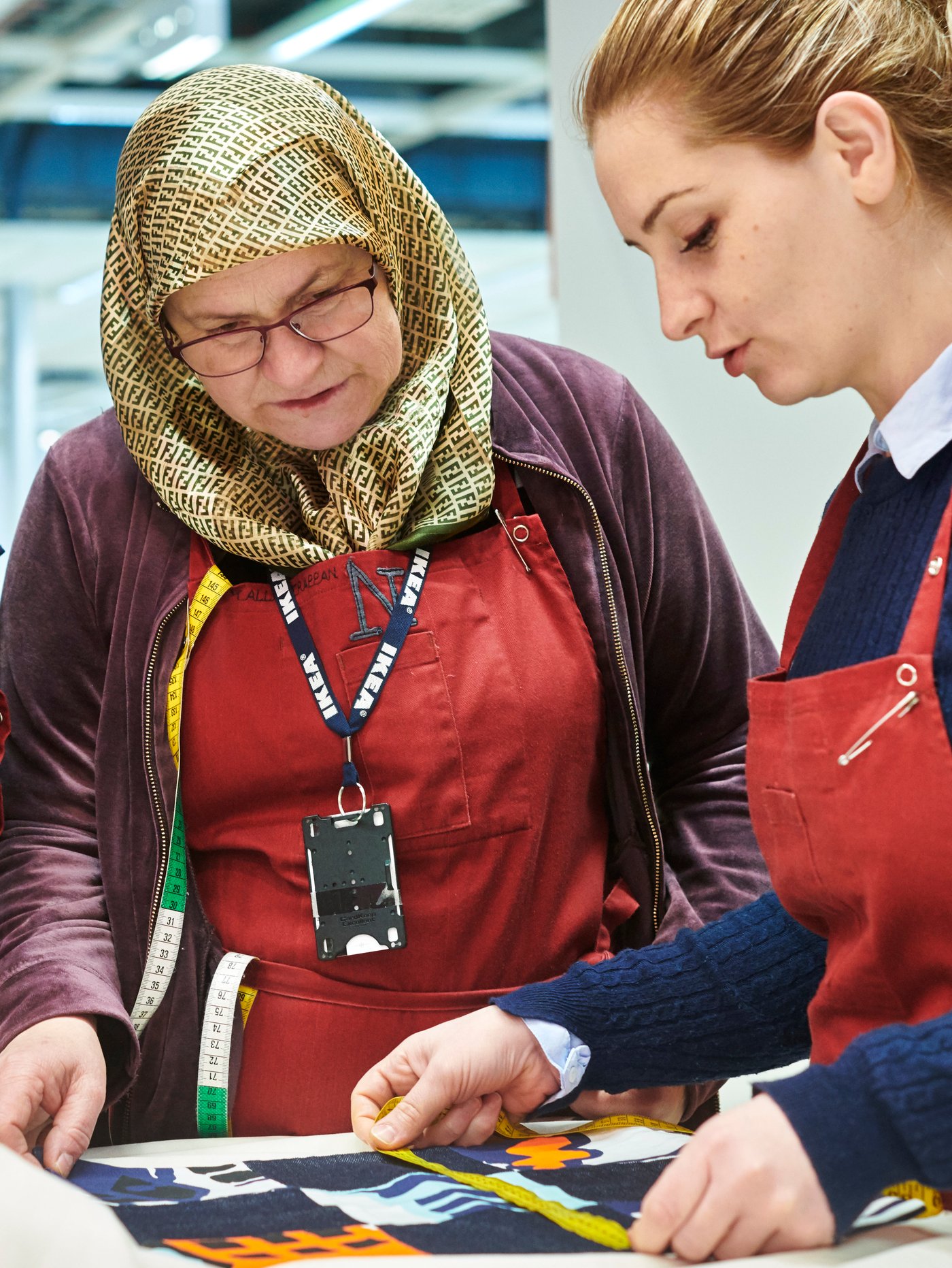 Two co-workers from Yalla Trappan sewing studio in the Malmö IKEA store in Sweden, measuring some fabric.