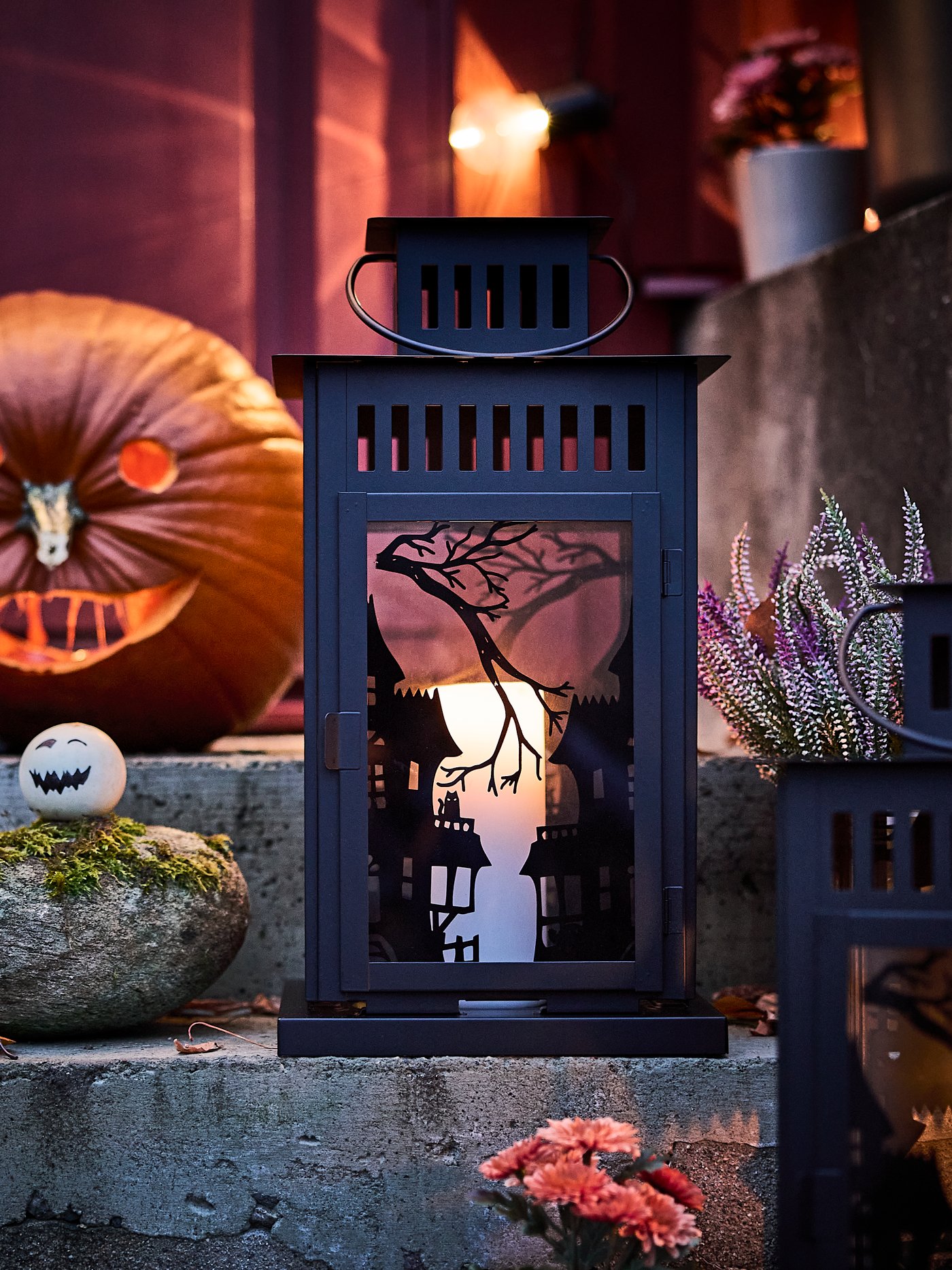 A Halloween-decorated outdoor staircase with a glowing pumpkin, and a lit candle inside a KUSTFYR lantern.