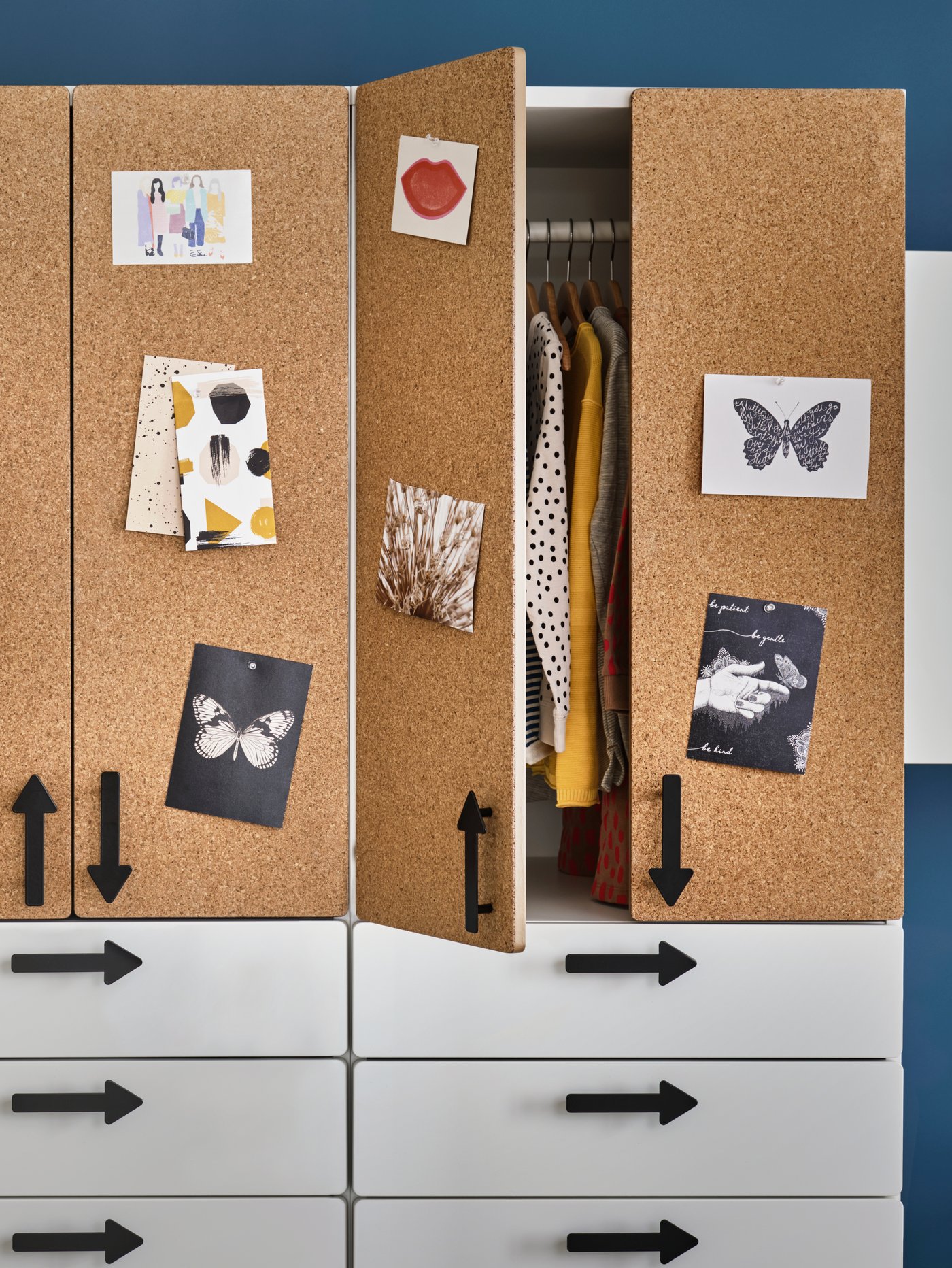 שני ארונות בגדים SMÅSTAD עם מגירות לבנות, דלתות מלוחות שעם וידיות בצורת חץ, ניצבים זה לצד זה. דלת אחד הארונות הבגדים פתוחה.