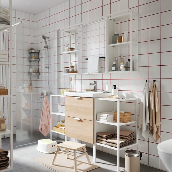 A natural wood and white ENHET bathroom vanity with black accessories in a bright white and beige bathroom.