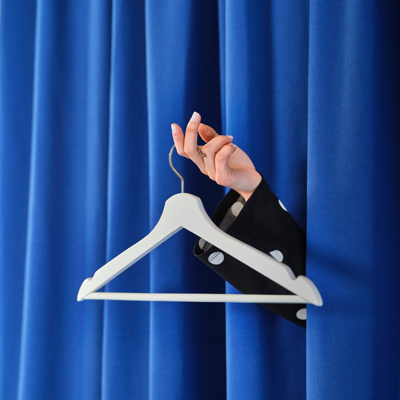 A hand emerges from behind a blue changing area curtain holding an empty BUMERANG clothes hanger.