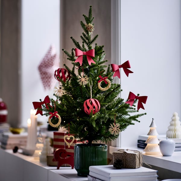 A small potted Christmas tree is decorated with red and gold VINTERFINT tree ornaments and is placed on a sideboard.