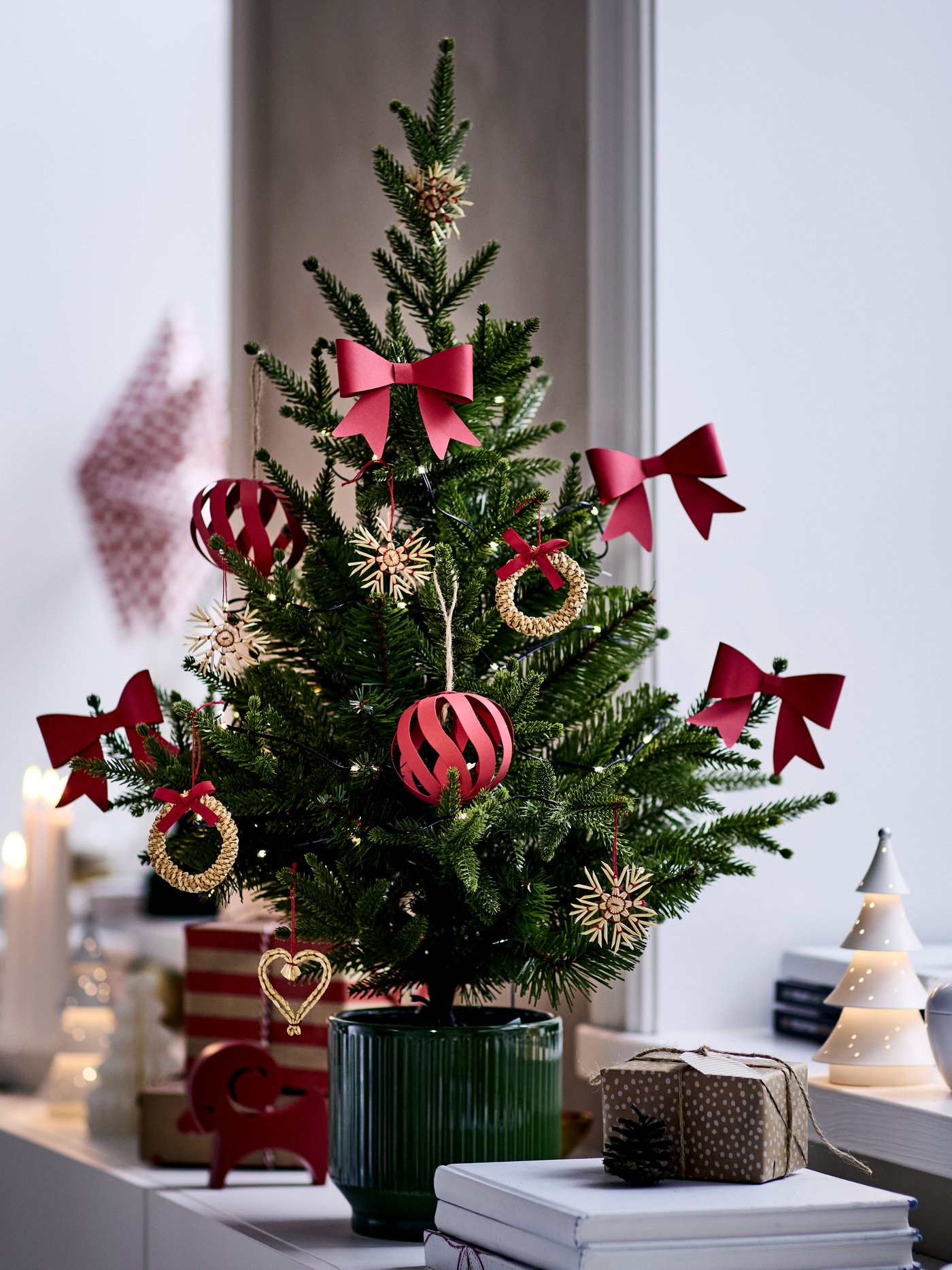 A small potted Christmas tree is decorated with red and gold VINTERFINT tree ornaments and is placed on a sideboard.
