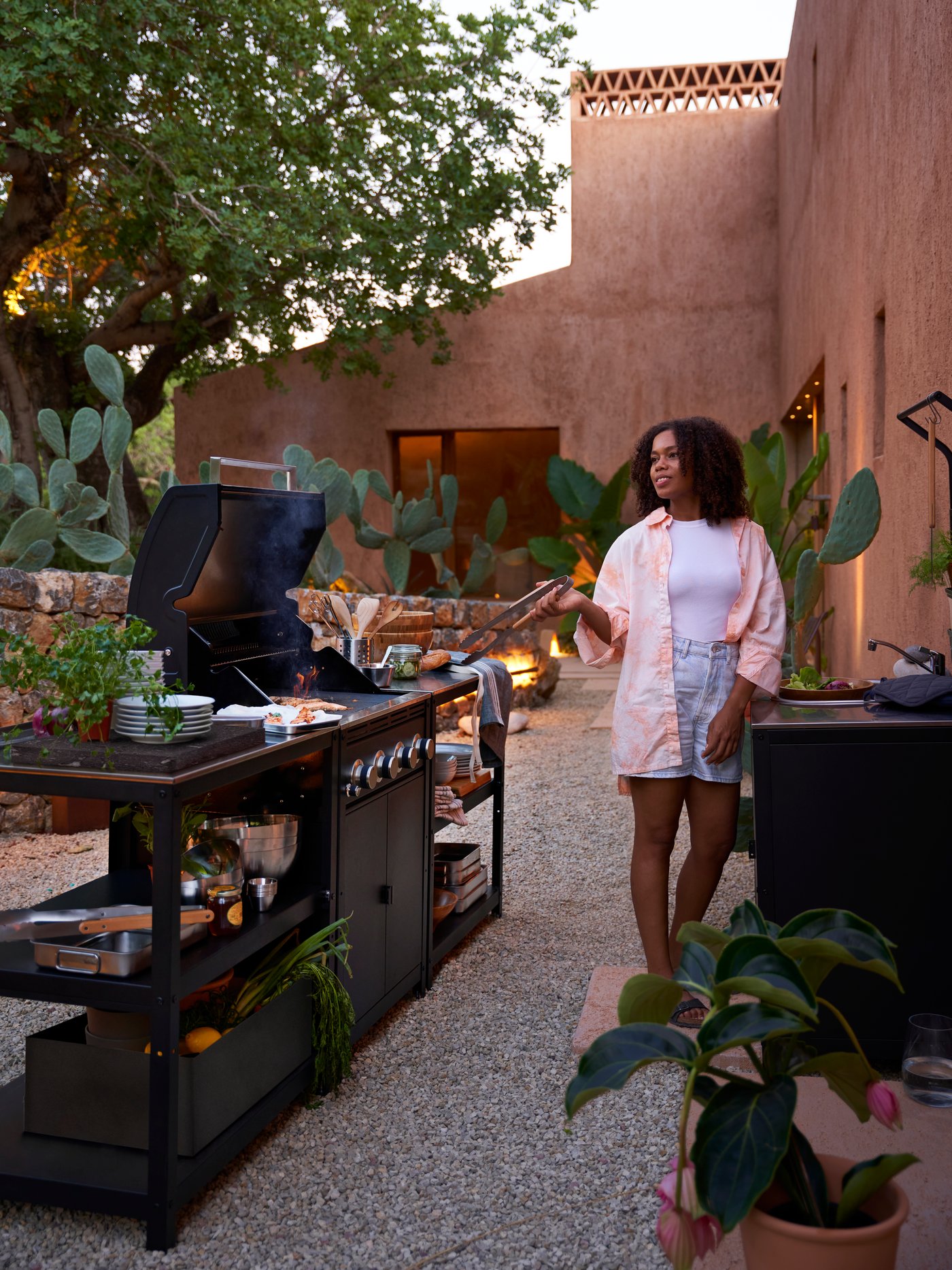 Exterior con una persona de pie junto a una barbacoa de gas GRILLSKÄR gris colocada entre 2 estanterías de isla de cocina GRILLSKÄR.