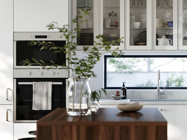 A kitchen with high-gloss RINGHULT fronts and wall cabinets with HEJSTA glass doors has a kitchen island in the foreground.