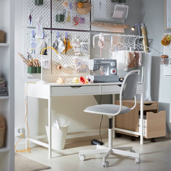 A white ALEX desk in a student room, with a drawer unit that has an opened drawer sitting next to it.
