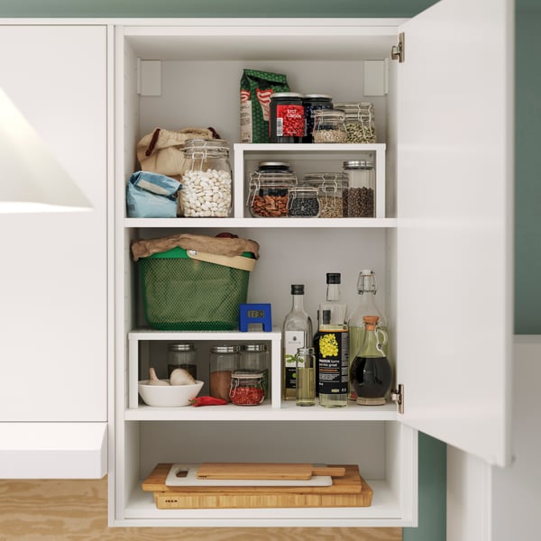 Un divisorio per ripiano VARIERA bianco su cui sono appoggiati contenitori e bottiglie, perfettamente organizzati nel mobile di una cucina moderna, pieno di prodotti alimentari.