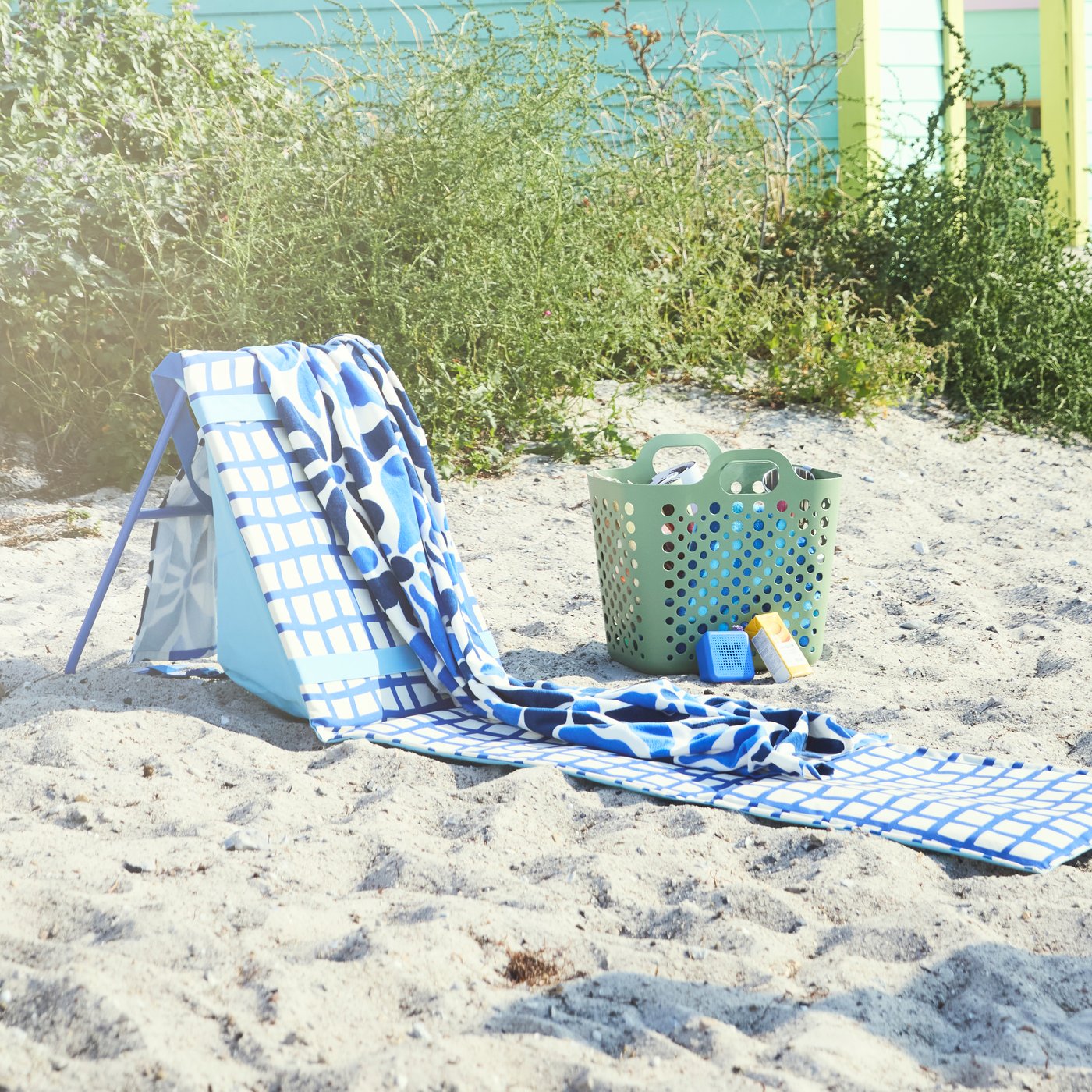 STRANDÖN sun lounger in blue and white set up on the beach with a towel on top, ready for you to relax and enjoy the sunshine.