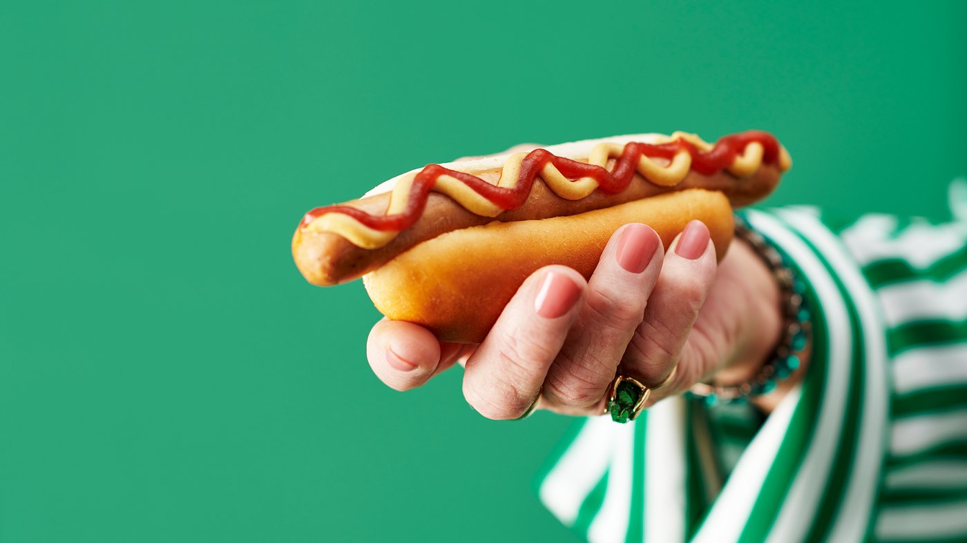 Käsi pitelee lihatonta hot dogia, jonka päällä on ketsuppia ja sinappia.