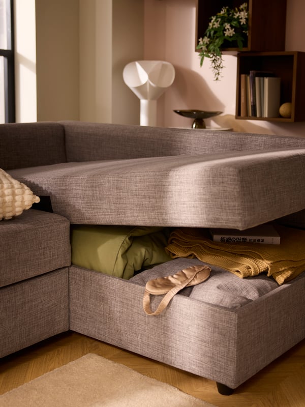 The gaping chaise-longue part of a FRIHETEN sofa-bed, revealing bedding and textiles placed in the compartment within.