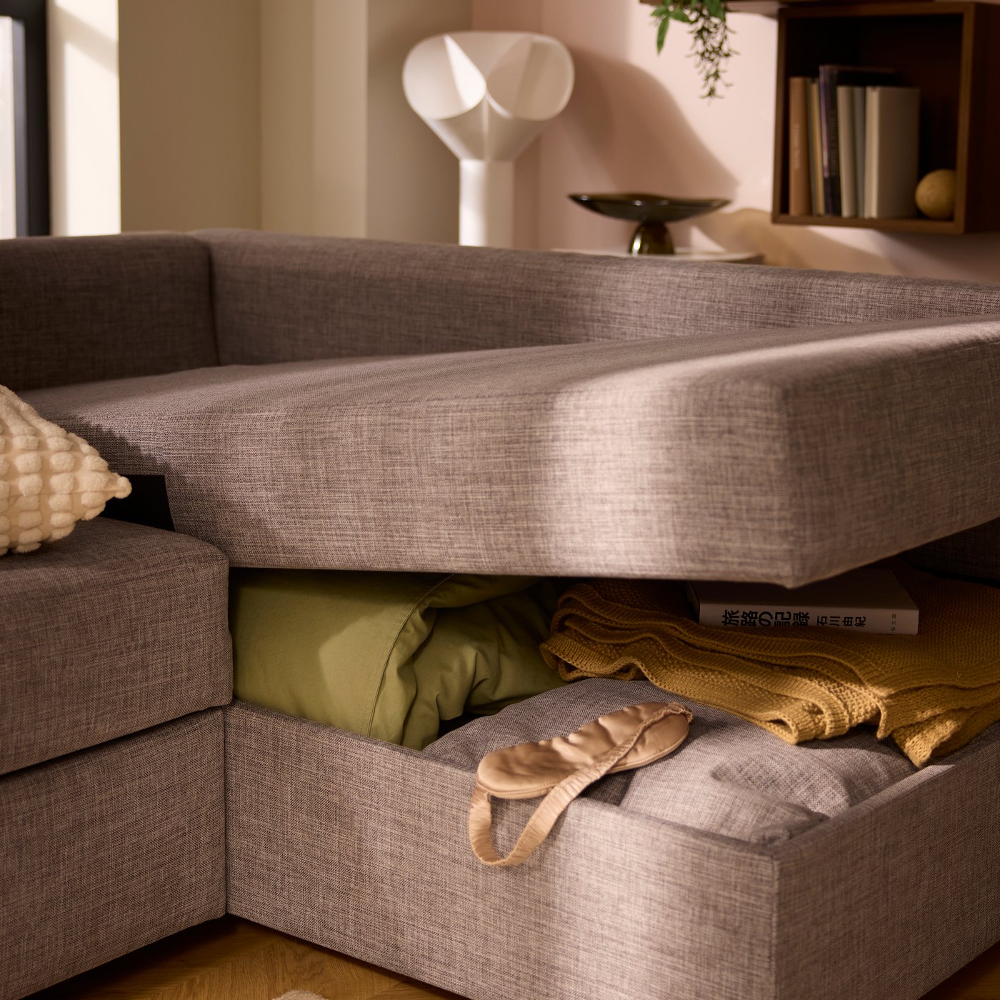 The gaping chaise-longue part of a FRIHETEN sofa-bed, revealing bedding and textiles placed in the compartment within.