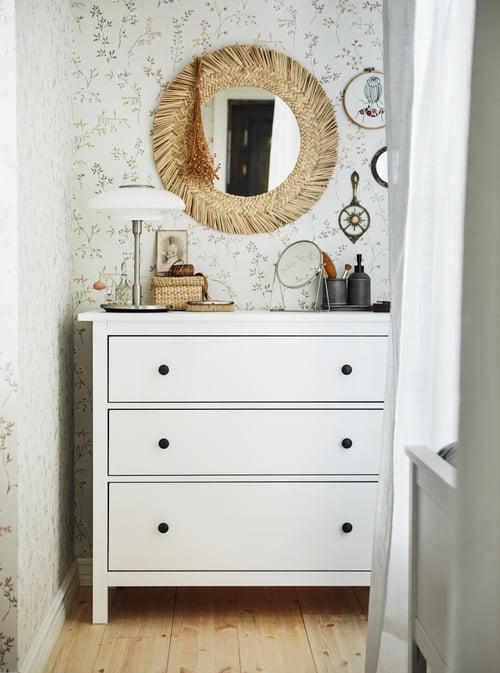 Bedroom with a white chest of 3 drawers made of solid pine, supporting a table mirror and a set of 2 boxes under a mirror.