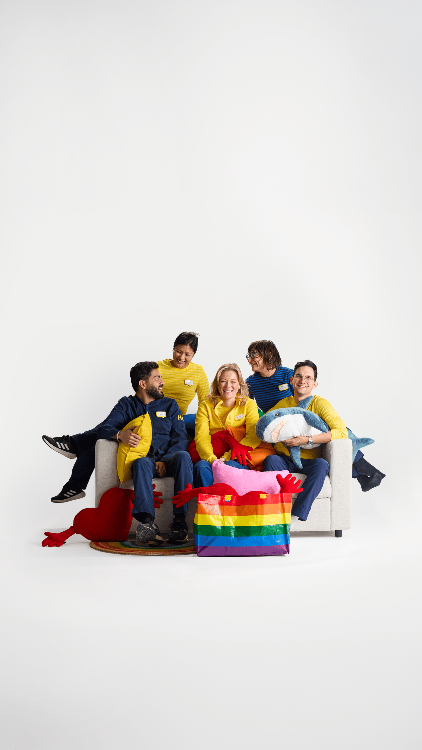 A group of IKEA co-workers sit together on a sofa with a rainbow-colored FRAKTA bag in front of them.