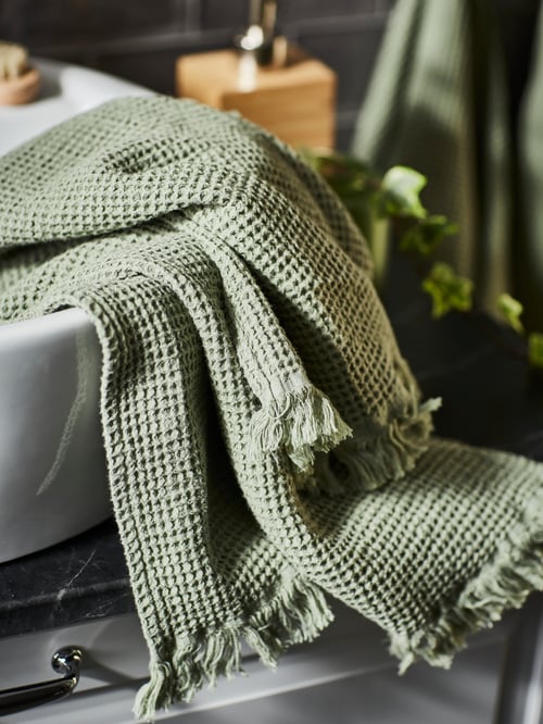 O fotografie de aproape a unui prosop de mână VALLASÅN de culoare verde deschis, cu design texturat, așezată pe o chiuvetă albă.