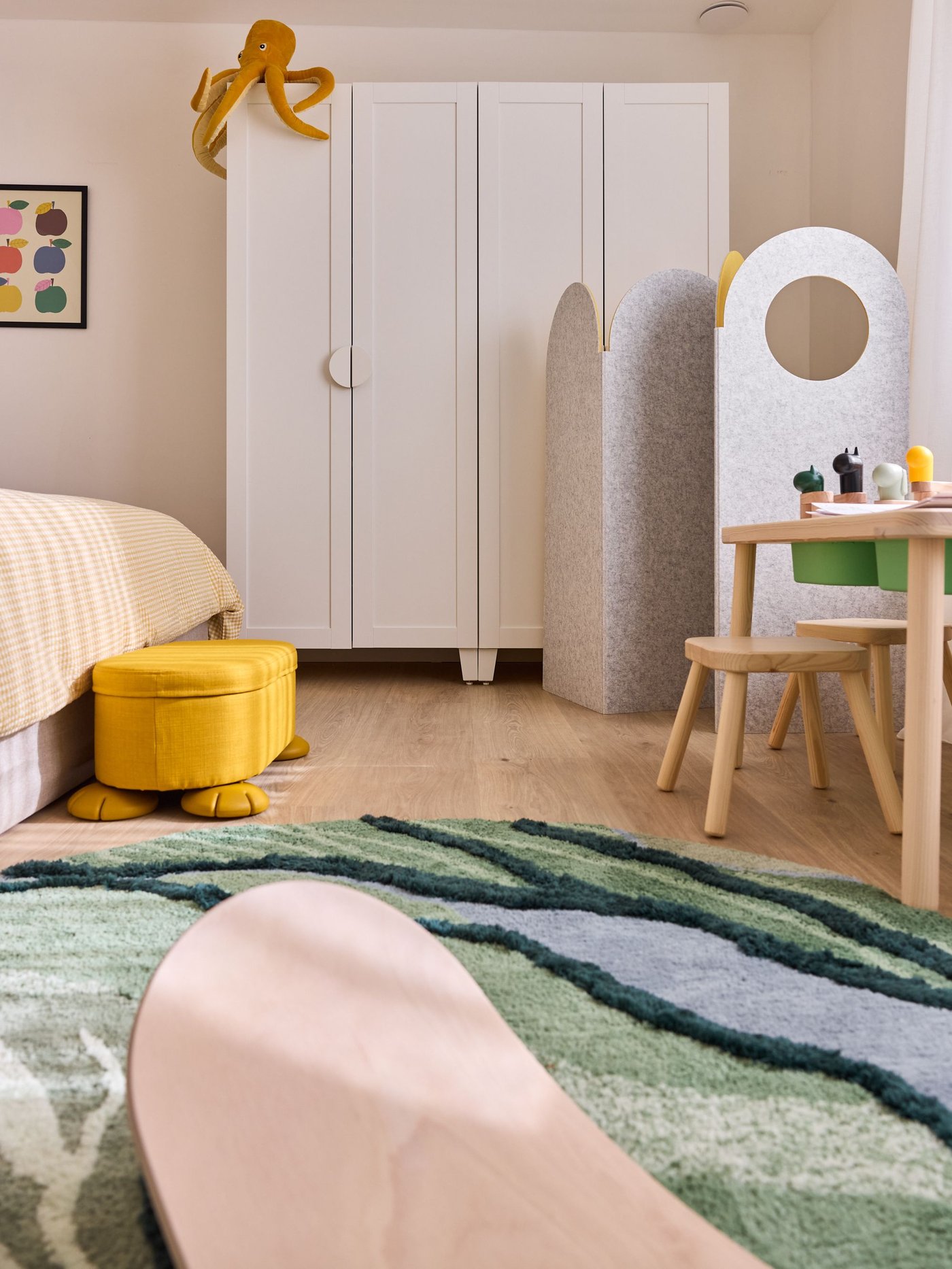 Kinderkamer met bed, speeltafel, kast en groen tapijt, speelse en warme sfeer met zachte materialen.