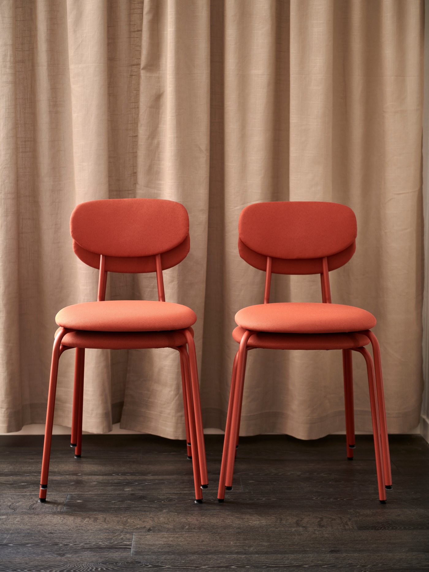 Fyra röda ÖSTANÖ stolar står framför en beige gardin.