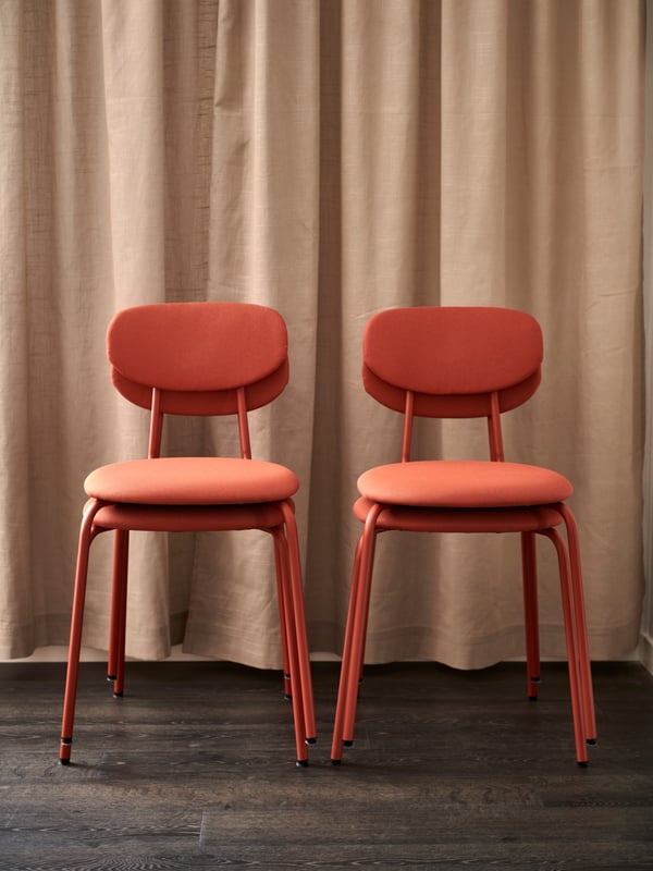 Fyra röda ÖSTANÖ stolar står framför en beige gardin.