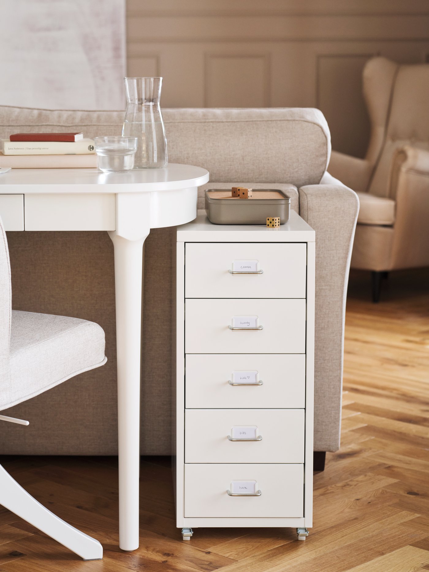A ROSENTORP swivel chair and a white HELMER drawer unit on castors stand at a white ROSENTORP desk behind a sofa.