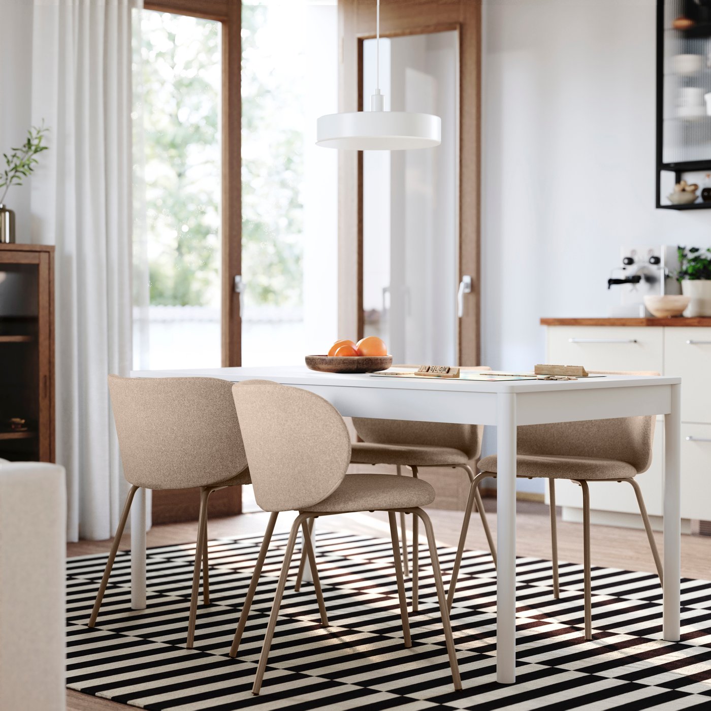 A modern dining area featuring a white table, beige chairs, and a bowl of oranges, set on a black and white striped rug. Spacious and bright.