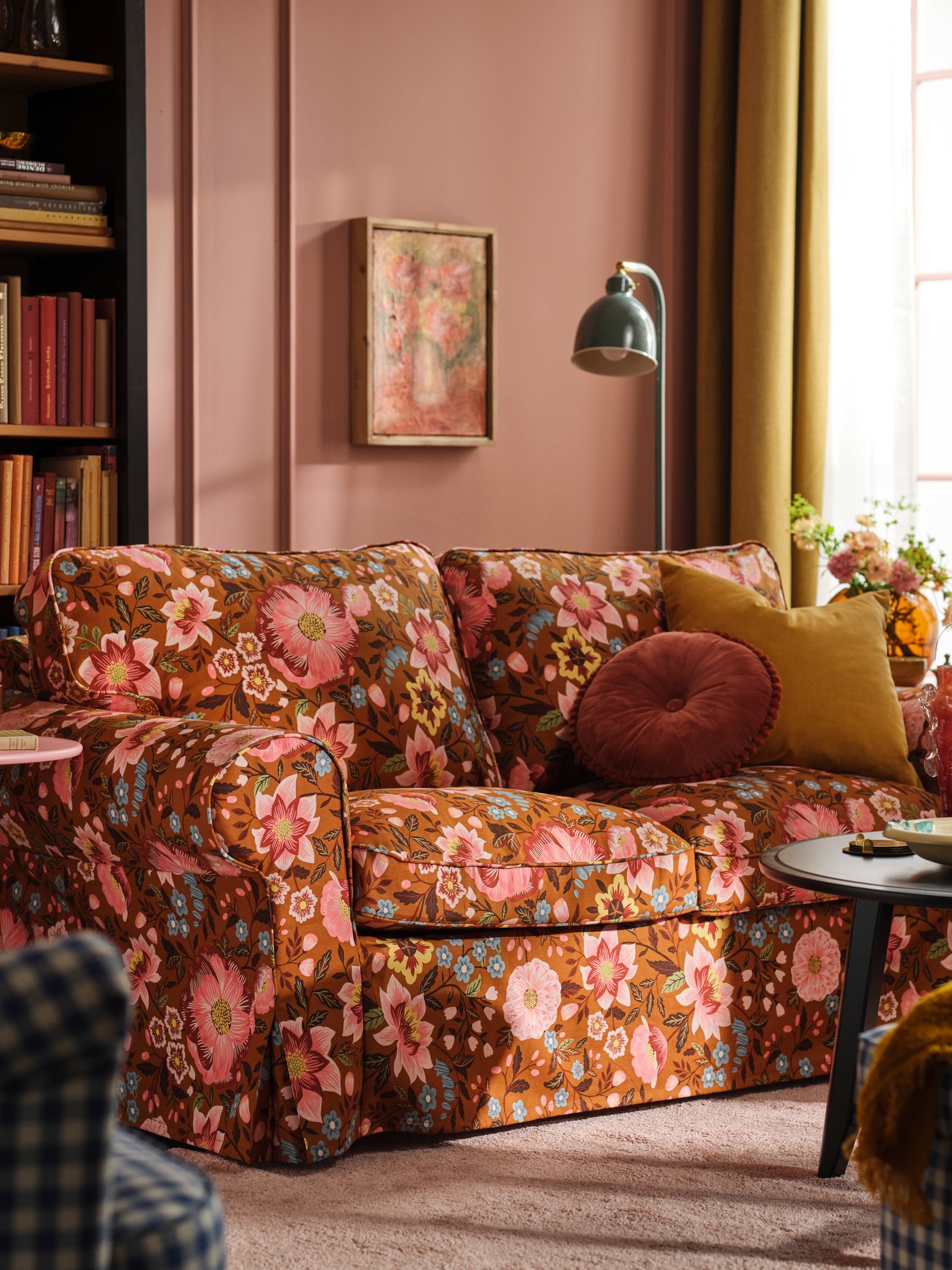 Pink living room with an EKTORP sofa fitted with a Mångbyn sofa cover in brown and multicoloured tones, placed in front of a bookshelf.