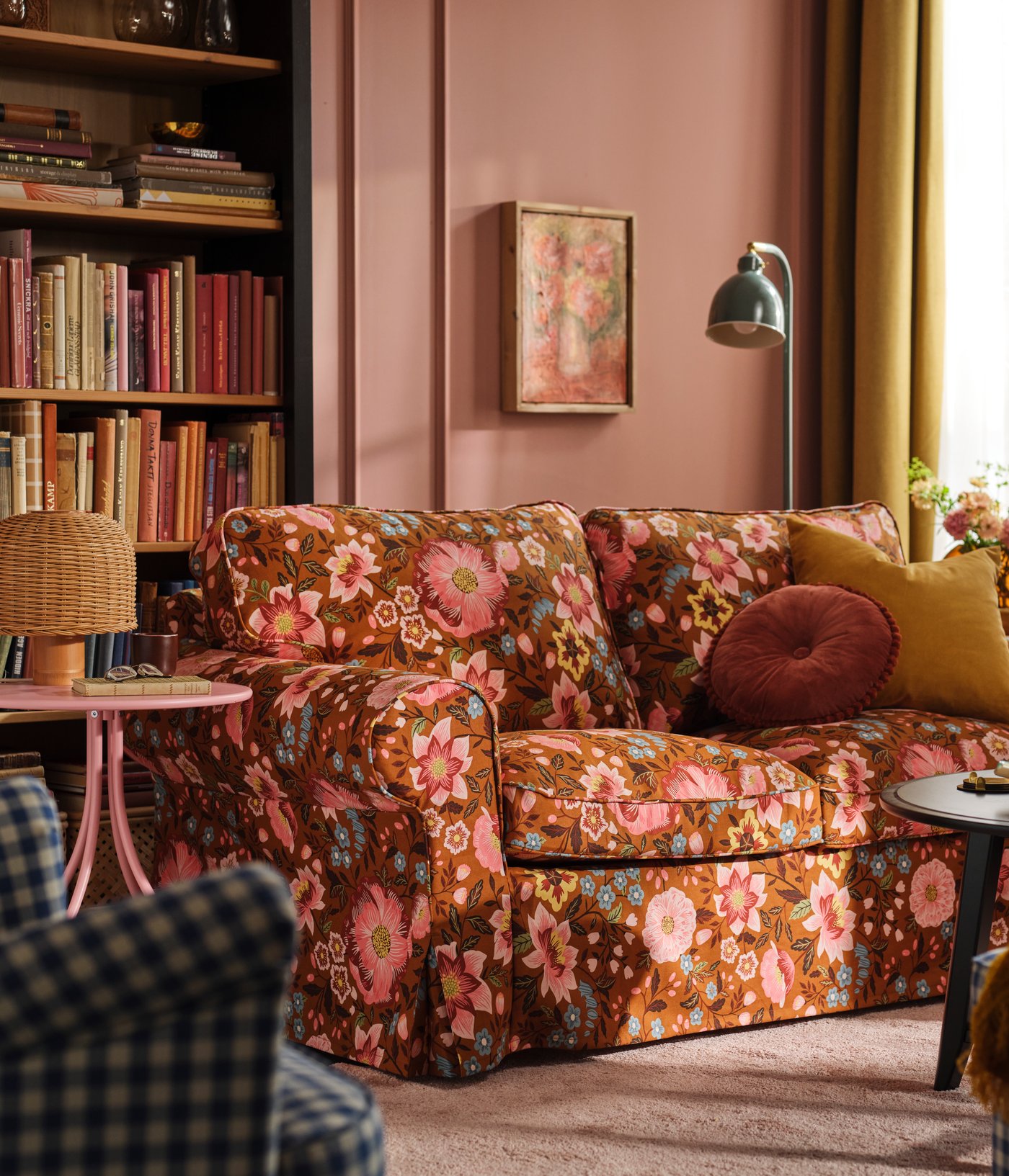 A pink living room with an EKTORP sofa dressed in a Mångbyn brown/multicoloured sofa cover in front of a bookshelf.