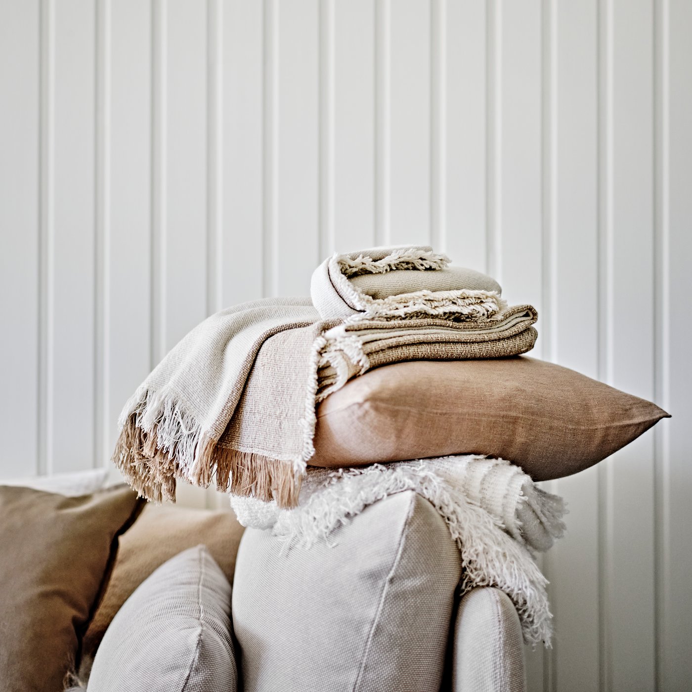 A cushion in a beige AINA cushion cover and an off-white EVALI throw on the arm of a light beige SÖDERHAMN corner section.
