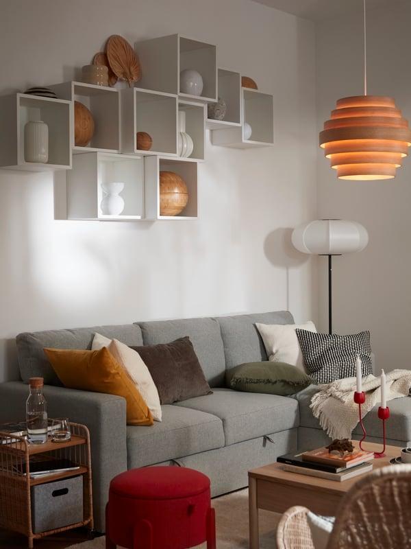 Part of a bright living room with a wall-mounted, artful arrangement of multiple EKET cube shelves over a BÅRSLÖV sofabed.