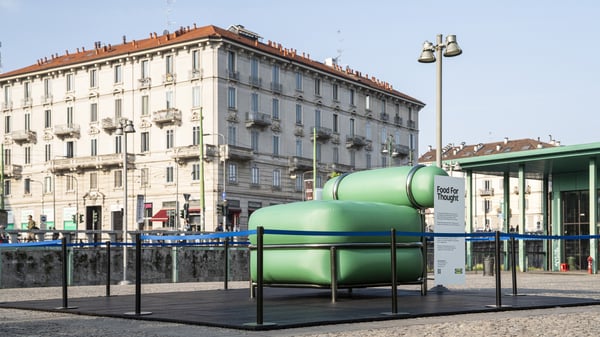Poltrona gonfiabile verde della nuova collezione IKEA PS 2026 esposta su una pedana all’aperto, delimitata da transenne, in una piazza cittadina di Milano. 