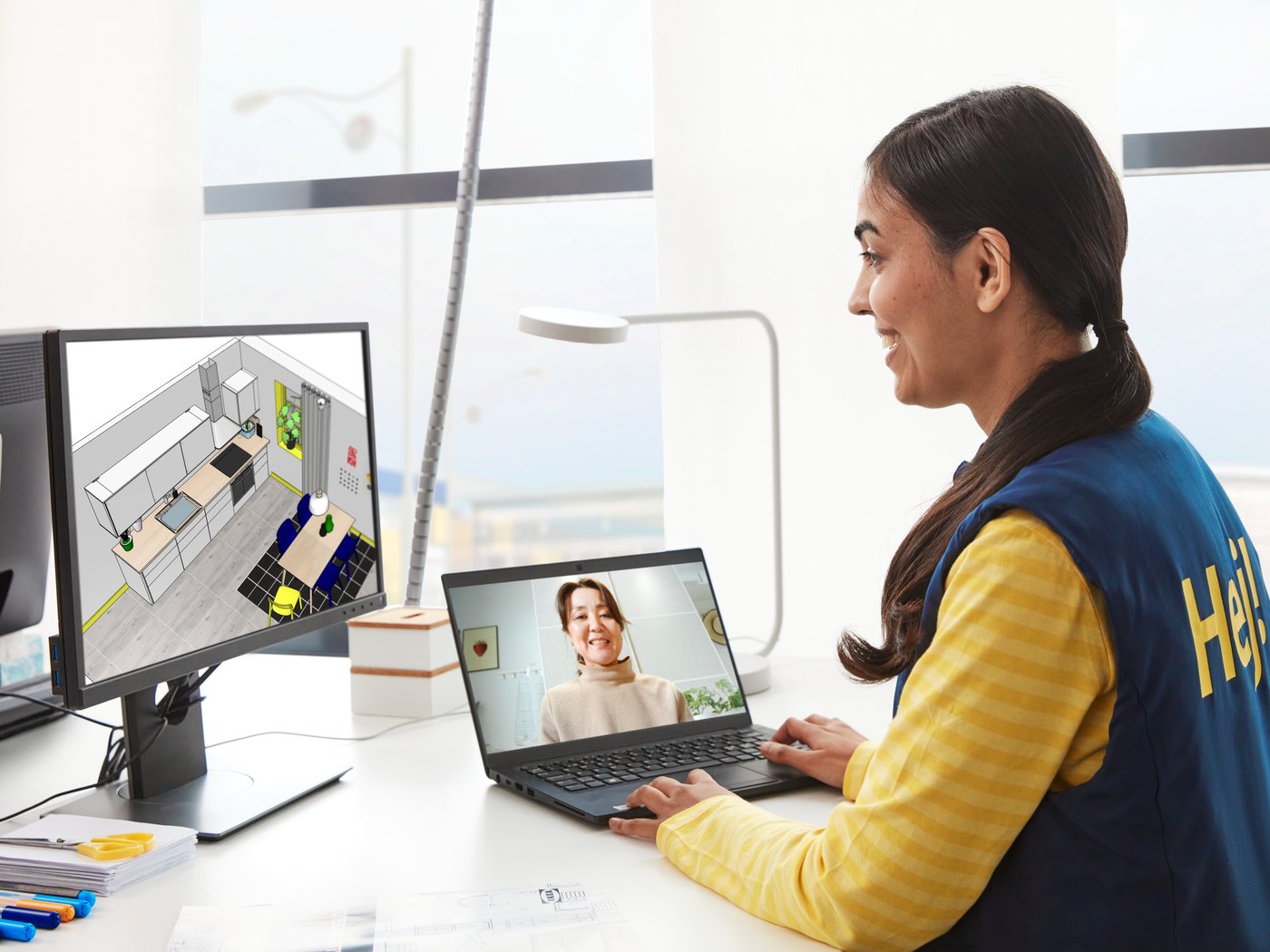 An IKEA employee is having a video call with a customer, while looking at a monitor with a kitchen.
