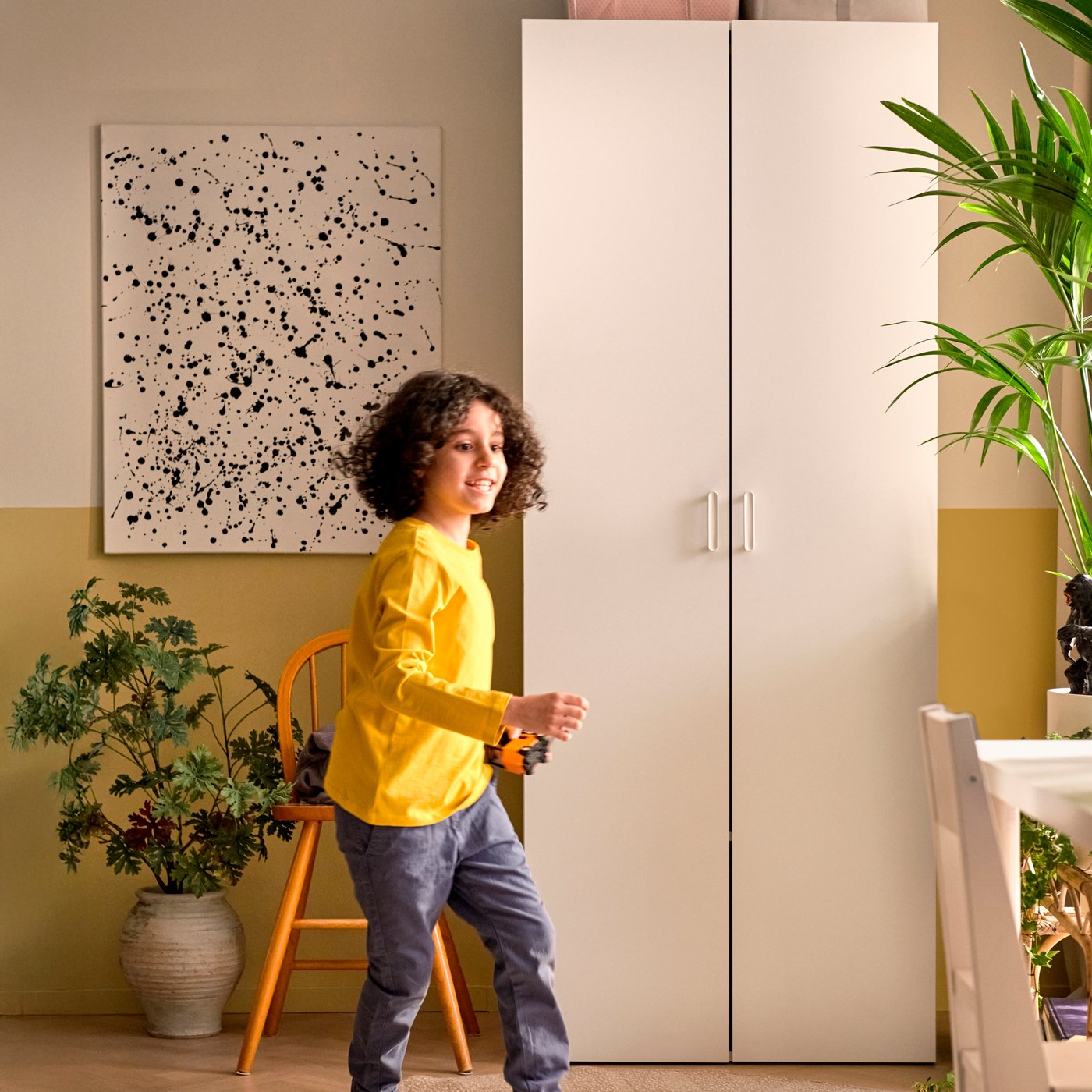 A white LASTARE wardrobe combination is closed and stands against a wall by a painting. A child is running in front of it.