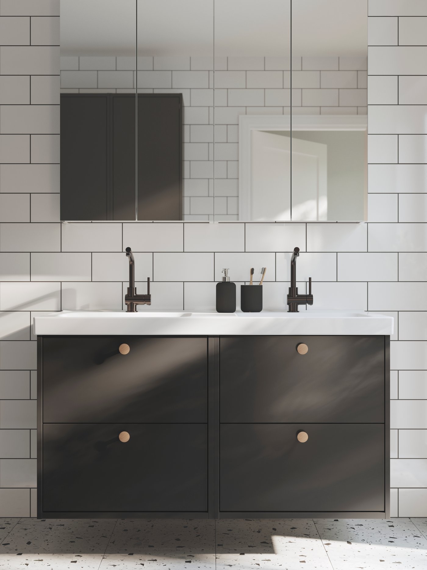 Ett badrum med vita kakelplattor och ett prickigt golv har mörkgrå HAVBÄCK tvättställ med vita handfat och spegelskåp.