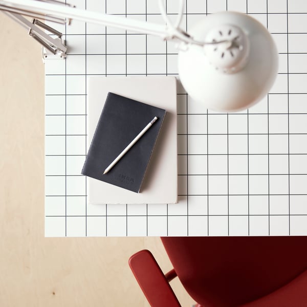 An aerial view of a white/anthracite checkered LAGKAPTEN tabletop, a red SMÖRKULL office chair, and a white TERTIAL work lamp.