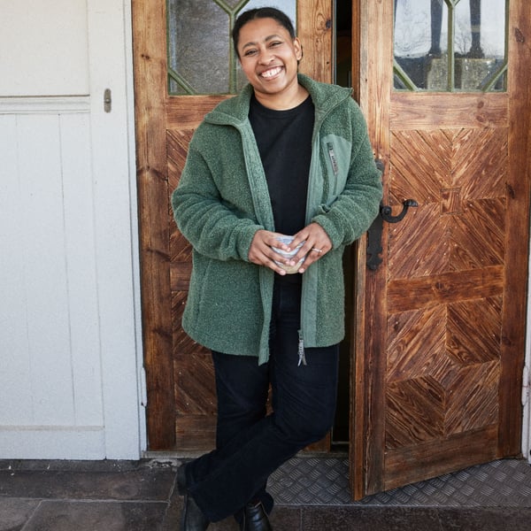 Alle with a cup of coffee in her hands standing by the front door smiling.