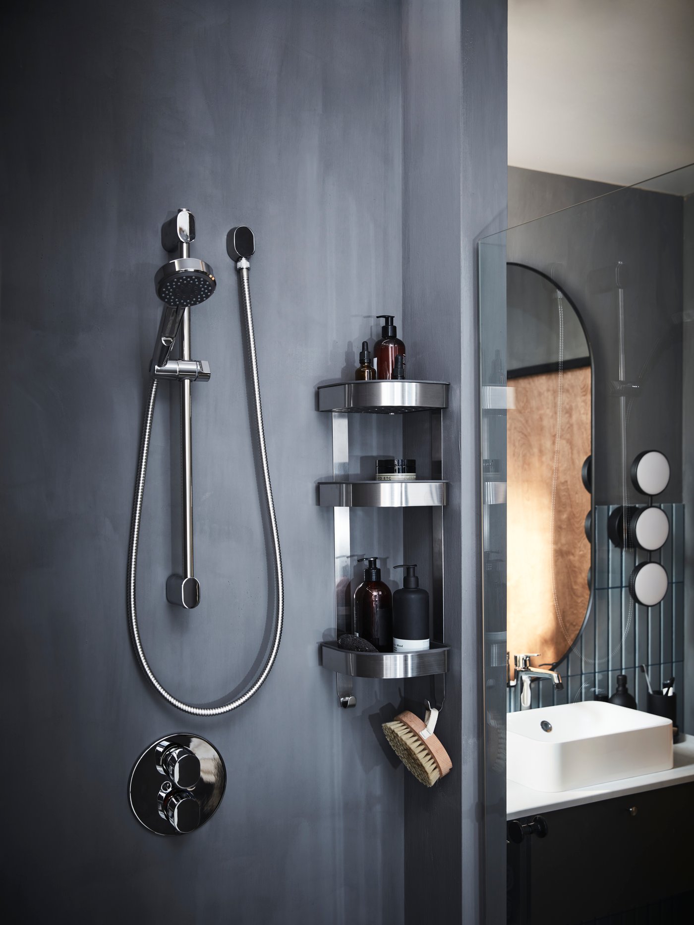 A softly lit grey bathroom with BROGRUND corner wall shelf unit of three shelves filled with soap bottles and a body brush.