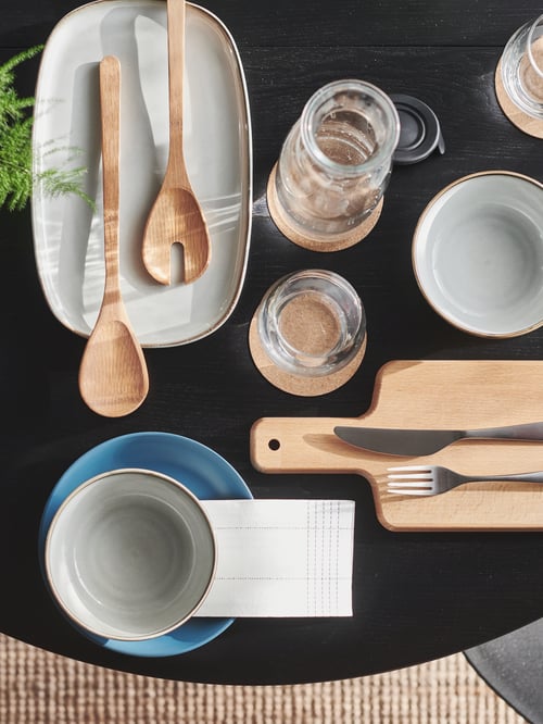 Top view of table with salad servers on large oval grey stoneware serving plate, blue plate, grey bowls, and glass carafe.