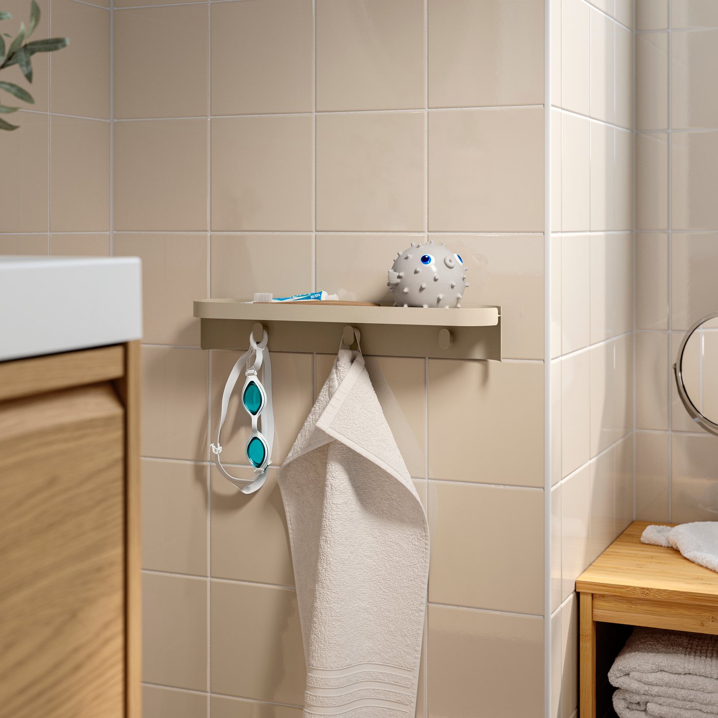 En blowfish-leksak står ovanpå en gråbeige FLORSJÖN vägghylla med tre krokar, i tvättställsnivå på en kaklad badrumsvägg.