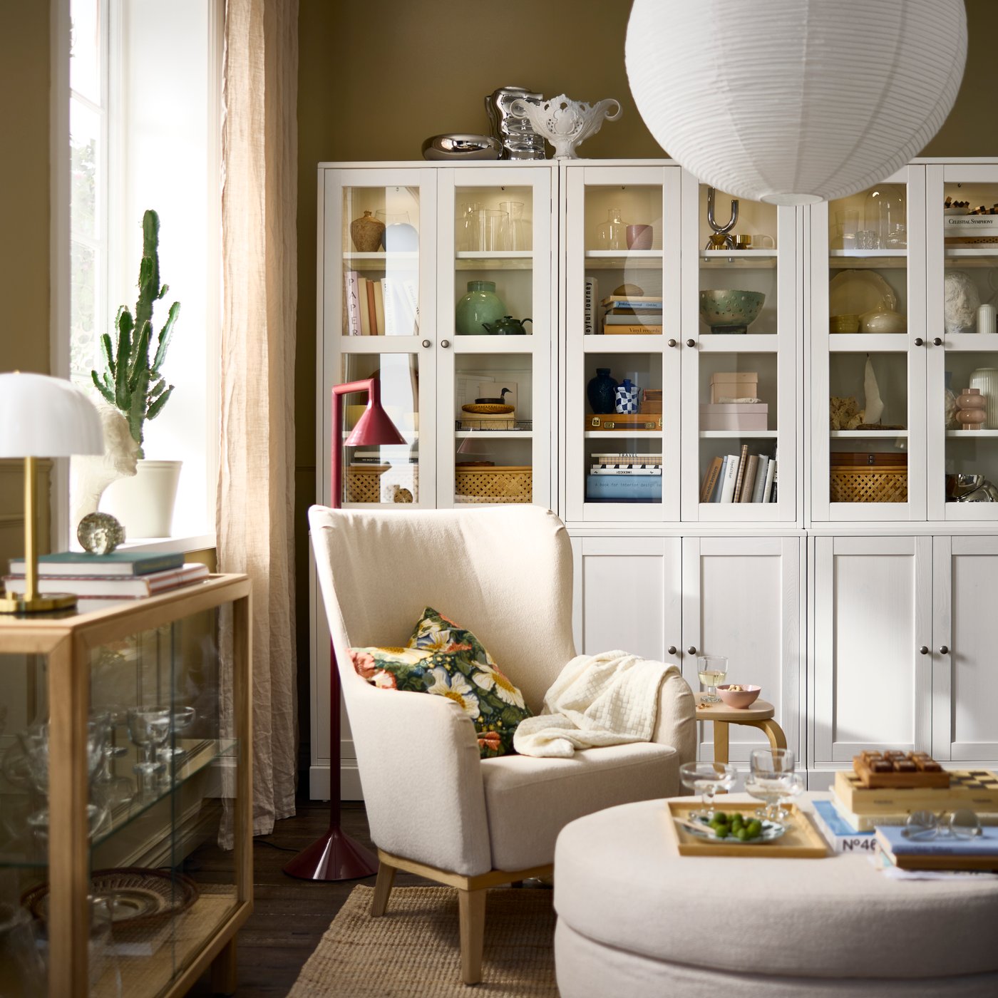 A living room featuring a white HAVSTA storage combination with glass doors, arranged with decorative items and plants.