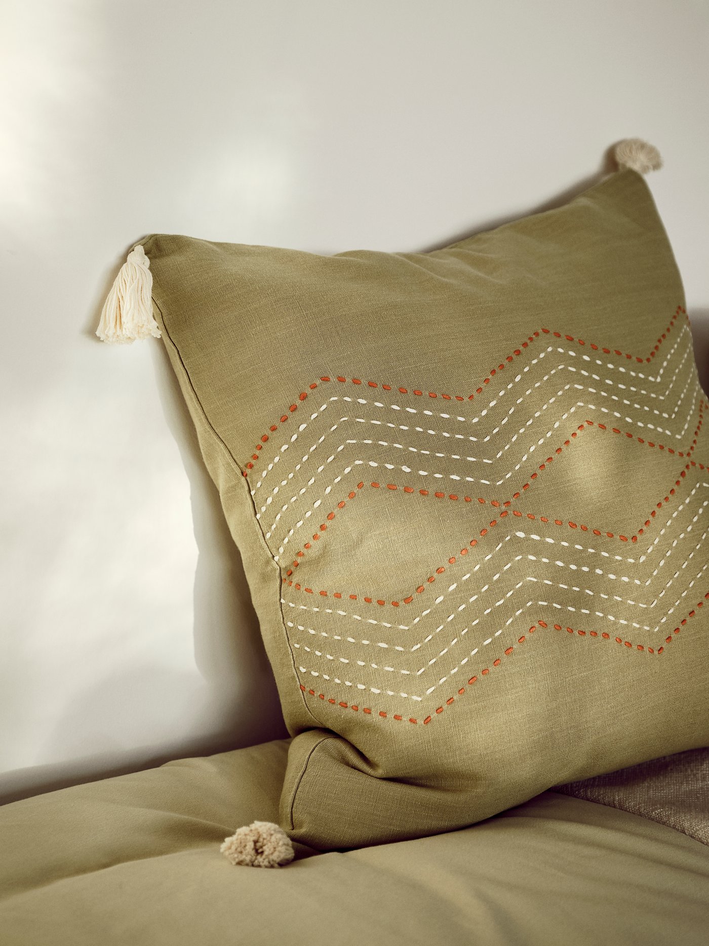 Details of handmade stitching and cream decorative tassels on the green HALLVI cushion cover.