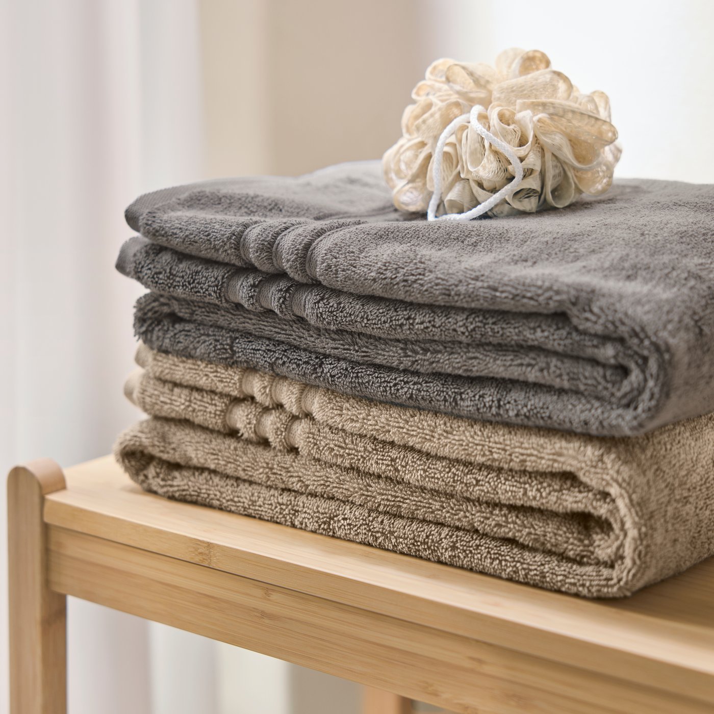 A close-up of neatly stacked bath towels in grey and beige on a wooden shelf in a bathroom setting.